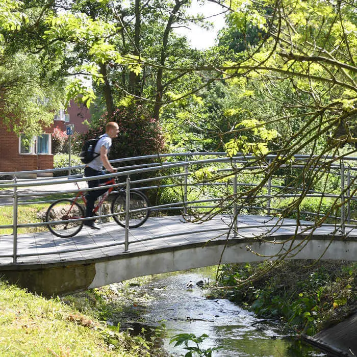 student crossing River Pinn bridge with a bycicle