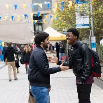 two students smiling and greeting each other with a handshake on brunel campus
