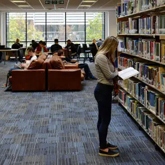 female student standing and reading by the bookshelves in the Brunel Library