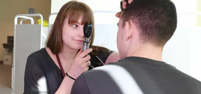 Female health student using an ophthalmoscope to look into patients eye.